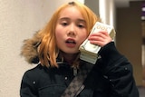 Little girl wear coat with fur jacket and holds up wad of cash