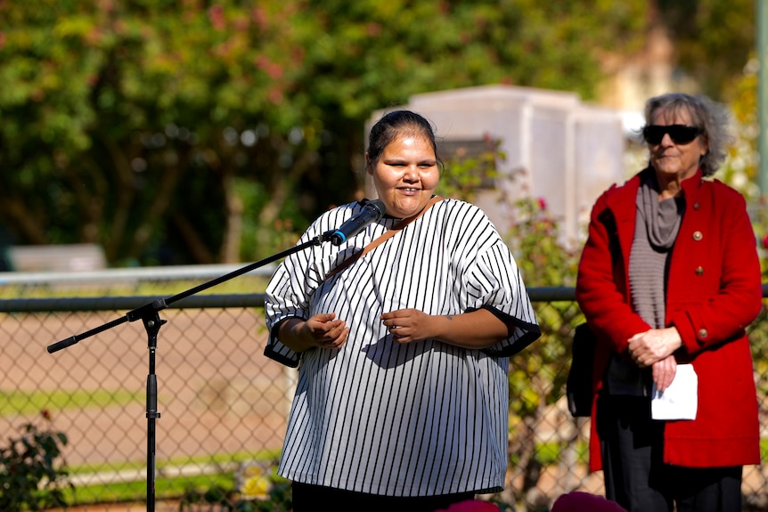 A Wilyakali aboriginal woman standing in front of a microphone who is wearing a striped shirt