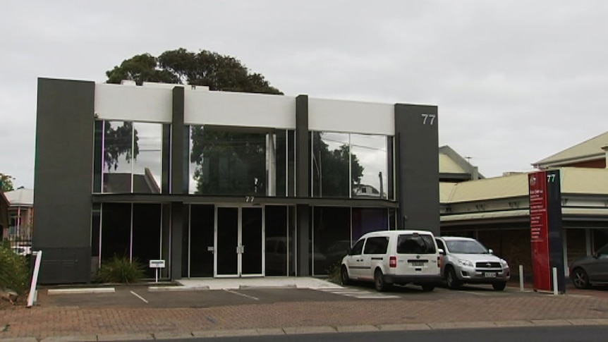 A two-story concrete rendered building with two cars parked out the front.