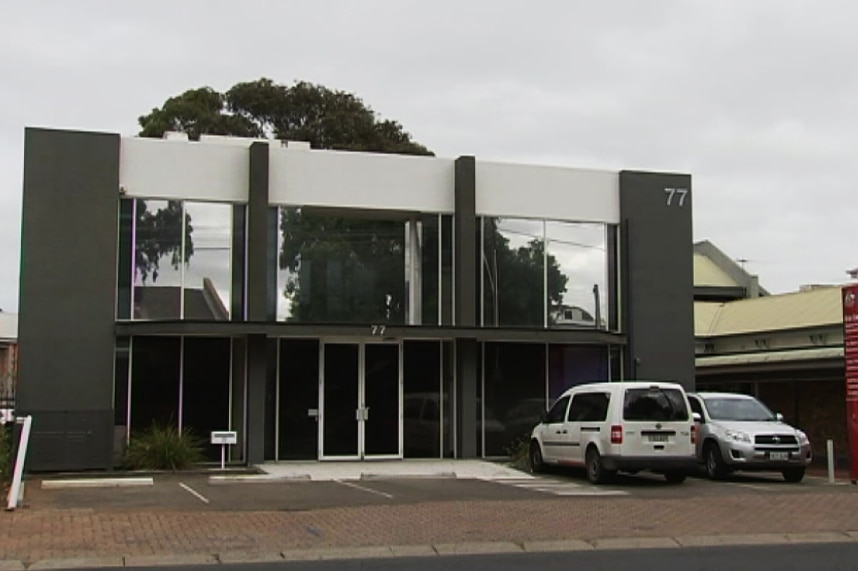 A two-story concrete rendered building with two cars parked out the front.