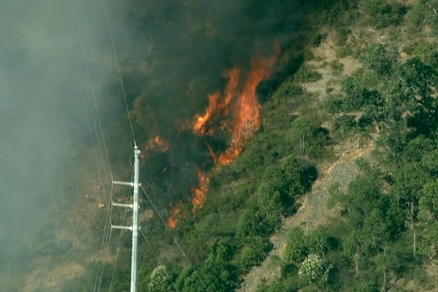 An aerial shot of fire burning through rocky terrain close to powerlines