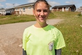 A young woman in a yellow t-shirt standing outside a house