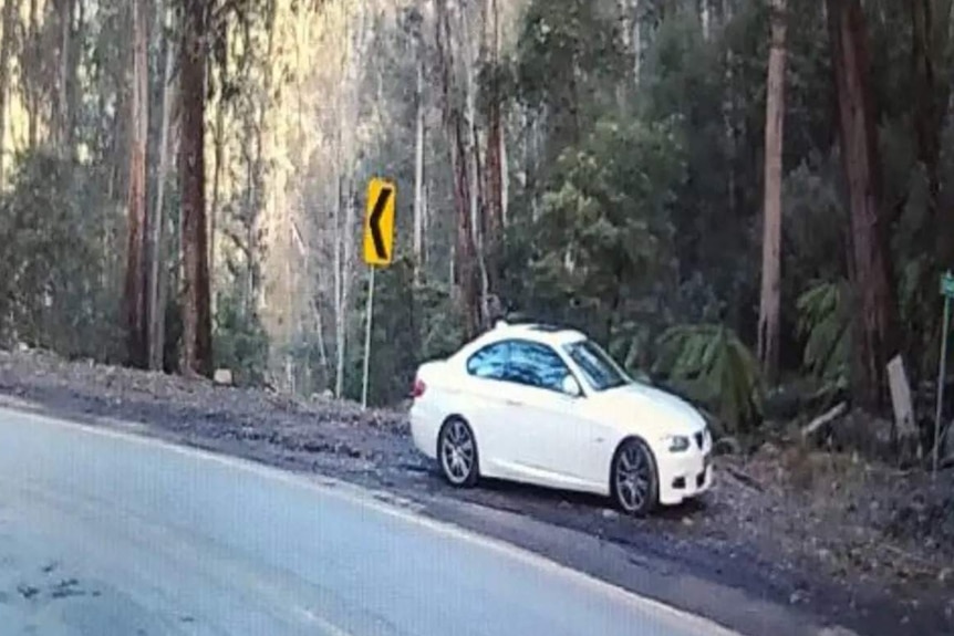 A white car is stopped on the side of road, along a bend.