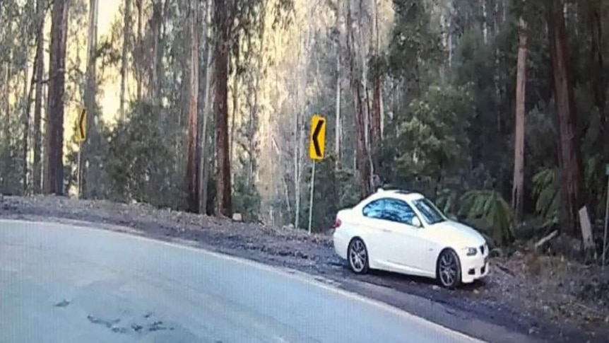 A white car is stopped on the side of road, along a bend.