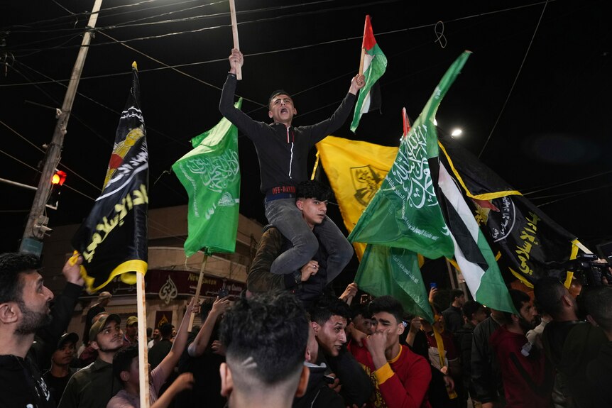 A man sits on the shoulders of another man as Palestinians dance in the street to celebrate ceasefire the announcement.