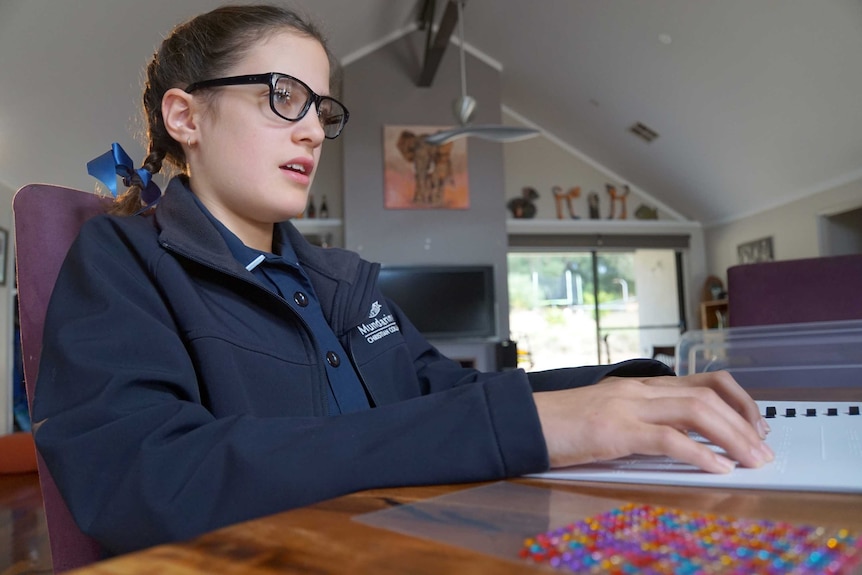 Caitlin Hannen-Williams sitting at a desk as she learns braille at home.