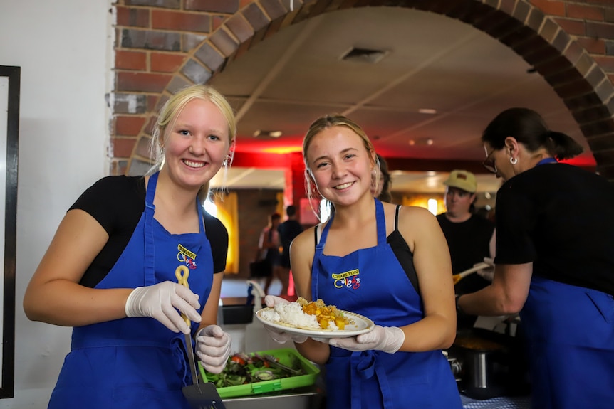 Two girls hold plate of food standing at service window through to motel