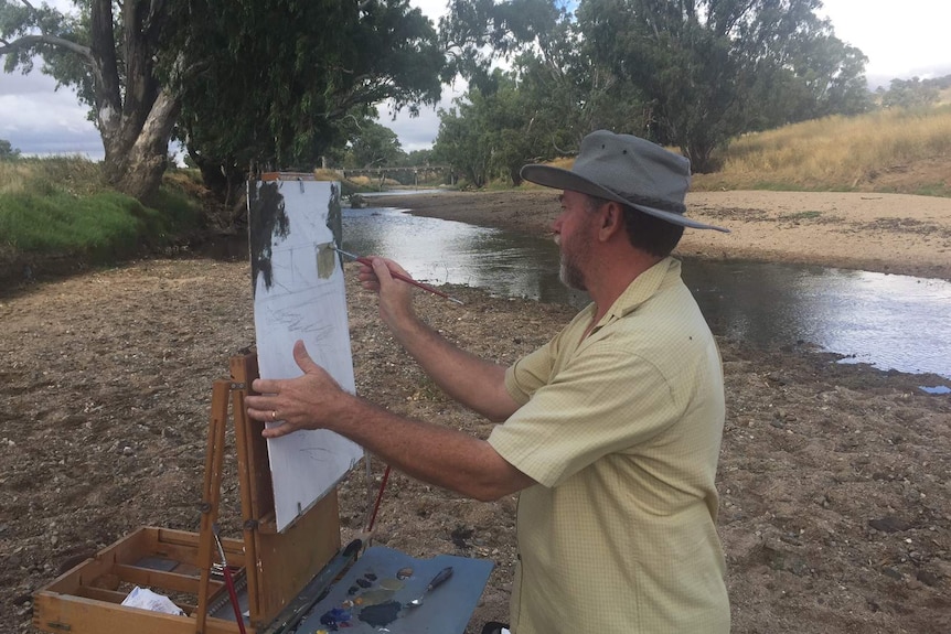 Garry Dolan at his easel, painting on the banks of a small river.