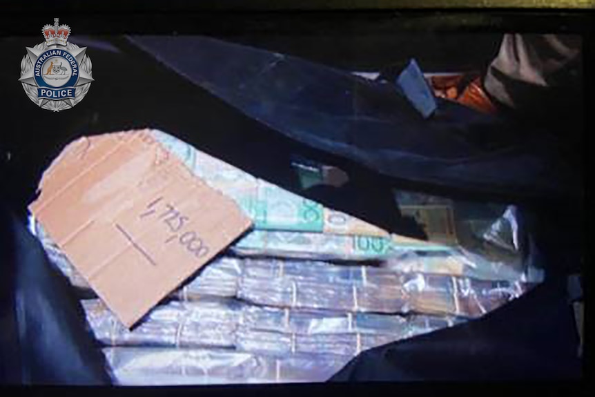 A black bag unzipped showing wads of $100 and $50 bills, with a piece of cardboard saying '1,725,000'.