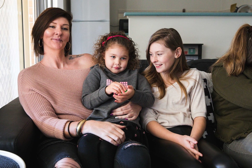 Christielee Plumridge sits on a couch with her daughters.