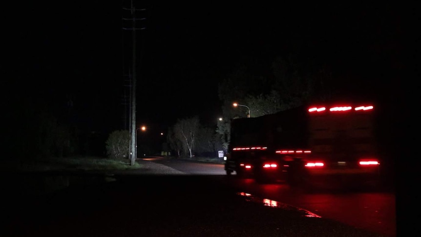 Red brake lights are visible as a truck drives down a quiet road at night.