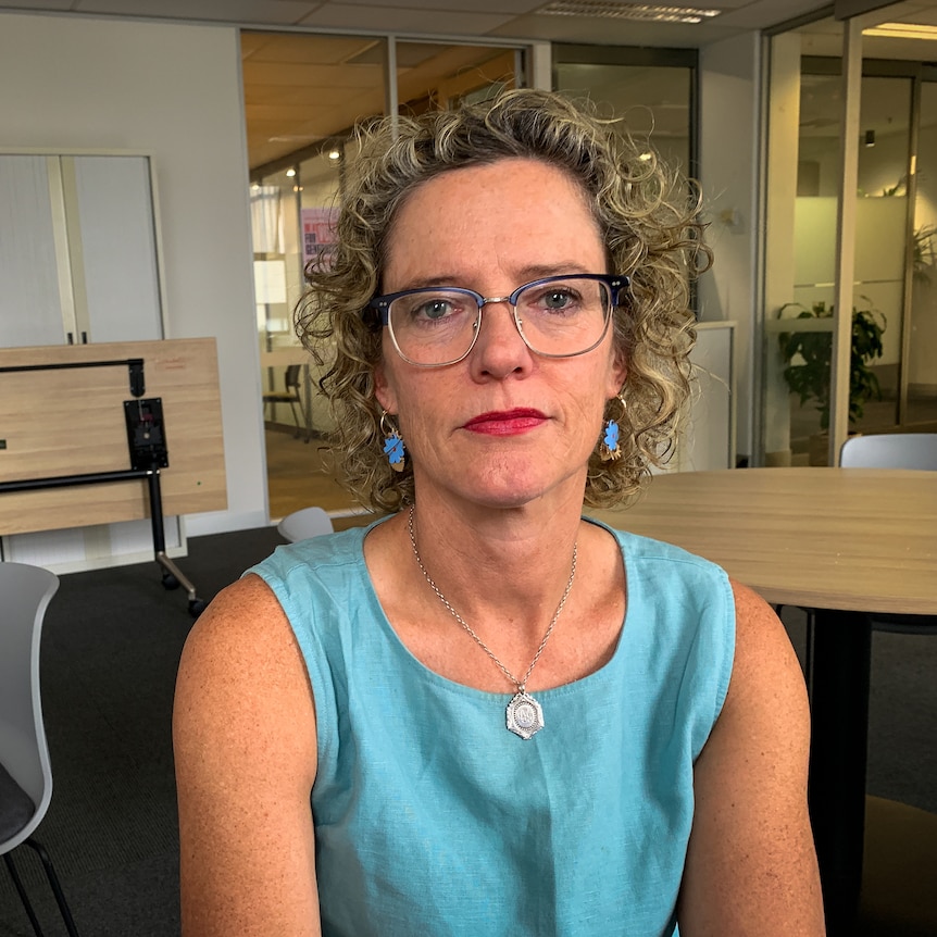 a woman wearing a blue top with curly hair and glasses in an office