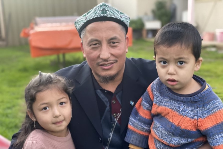 A man wearing a hat with a young girl and boy on his lap