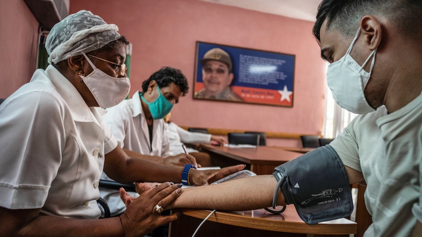 a man extends his arm and a health worker in a mask checks his blood pressure