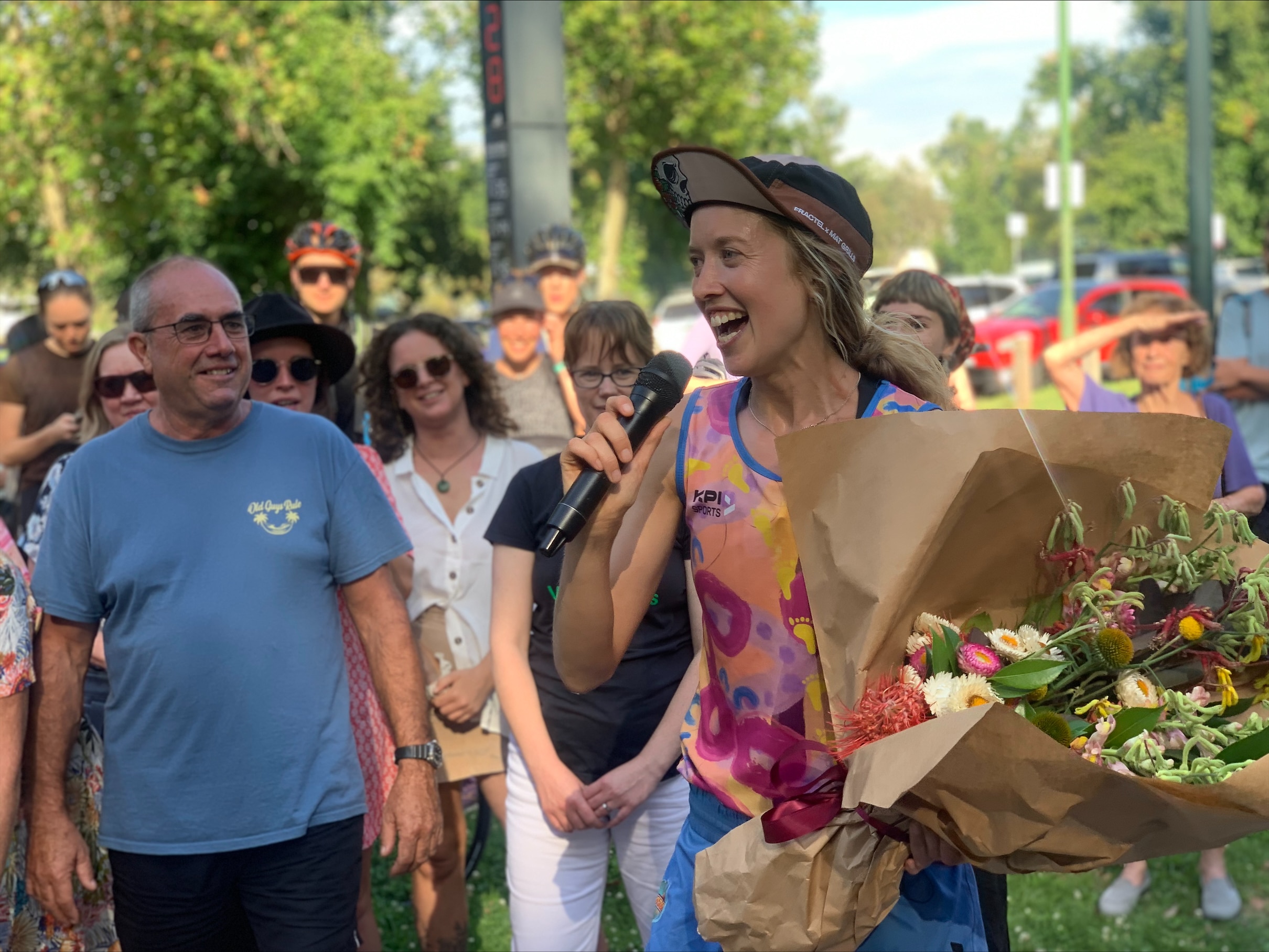 A woman smiles and holds a microphone and a large bunch of flowers.