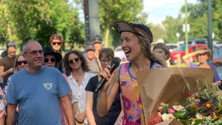 A woman smiles and holds a microphone and a large bunch of flowers.