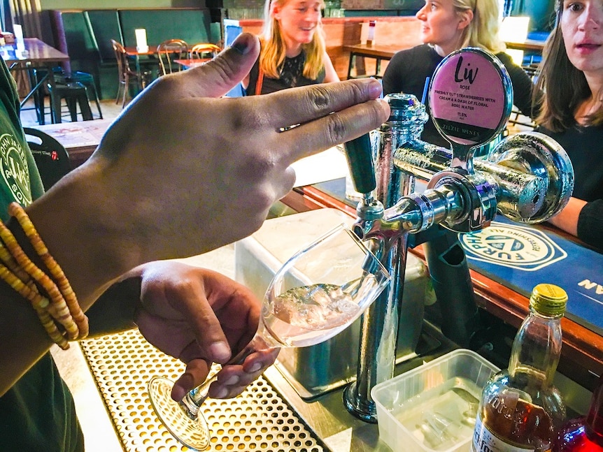 A glass of wine is poured at a bar using the same type of tap used to pour a beer.