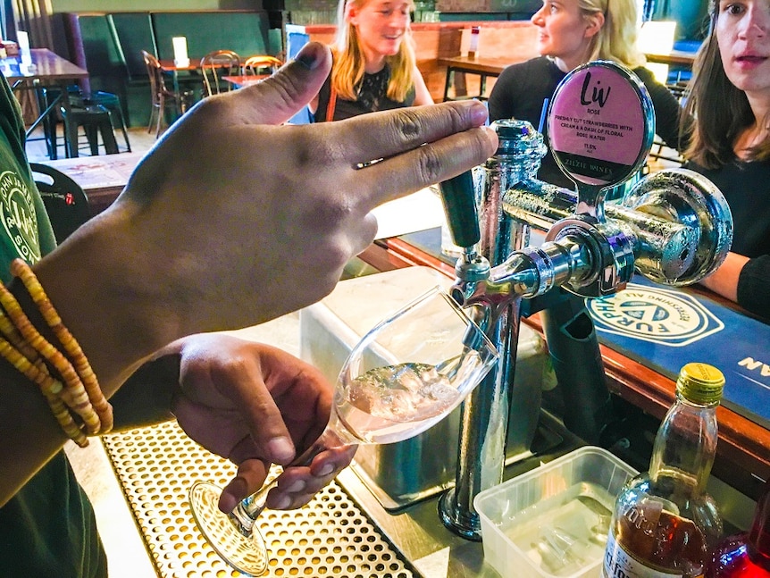 A glass of wine is being poured at a bar using the same type of tap used to pour a beer