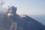 An image of the Kadovar Island volcano erupting, taken from a plane. There is thick smoke and ash rising from the island's top.