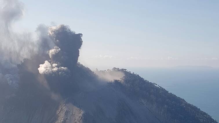 An image of the Kadovar Island volcano erupting, taken from a plane. There is thick smoke and ash rising from the island's top.