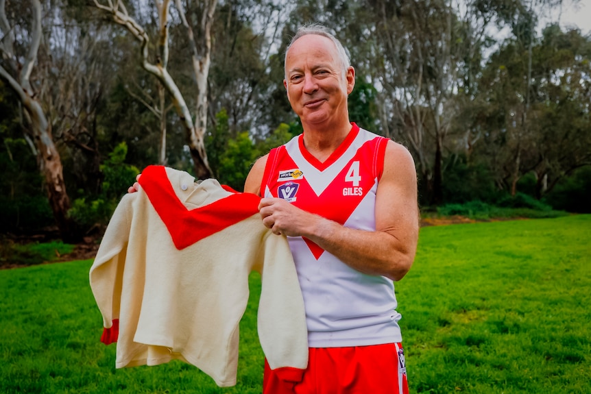 Giles holds a woolen jumper and smiles