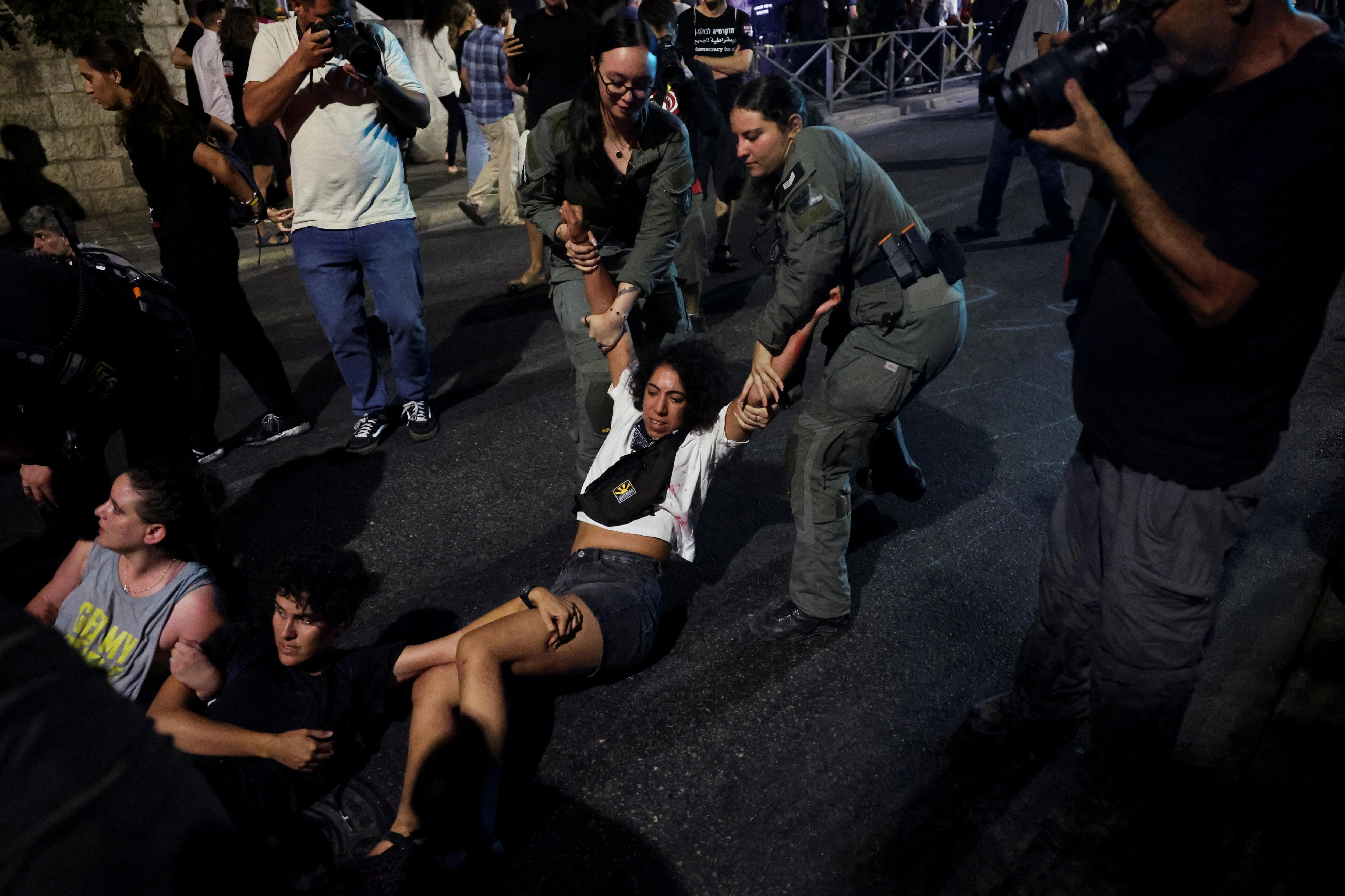 Two female police officers dragging a woman on the street while another person hangs on to her legs