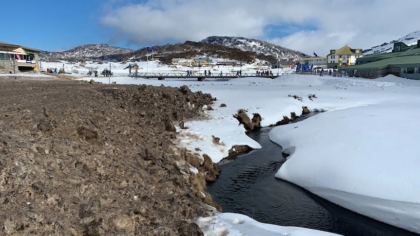 An alpine village, with snow in the foreground, and a creek