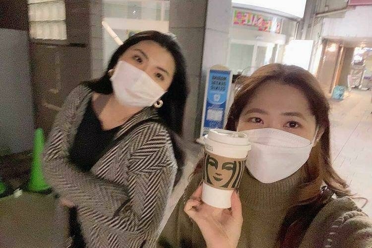 Two women wearing masks pose for a photo while walking on a footpath