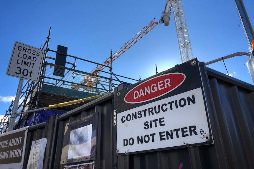 A danger sign on a metal fence with cranes in the background. 