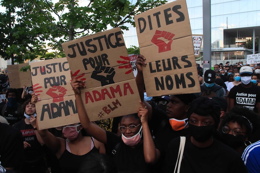 A group of people stand holding placards reading "justice for Adama" and "say their names", some in French.
