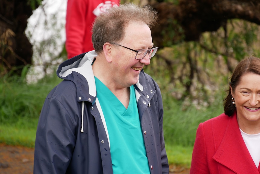 A man in a rain jacket and glasses next to a woman in a red jacket.