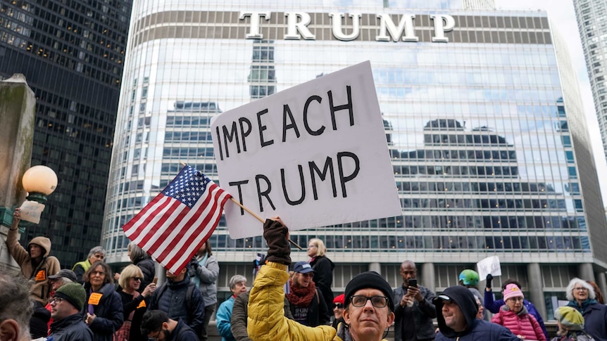 A protestor holds up a sign with Impeach Trump in front of Trump Tower in New York.