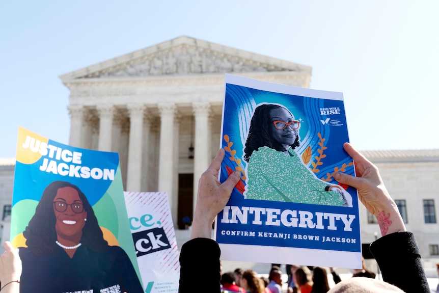A woman holds a colourful poster featuring Ketanji Jackson Brown up in front of the Supreme Court.