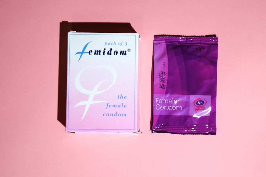 A female condom box and a female condom in its wrapper sitting against a pink background.
