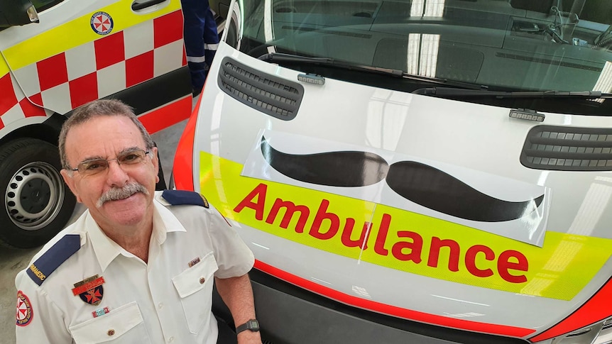 Image of Allan Spindler in his NSW Paramedic uniform standing beside the front of an Ambulance.