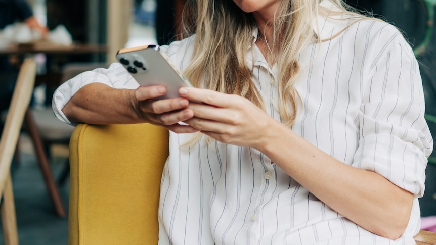 woman wearing white shirt looks down at phone