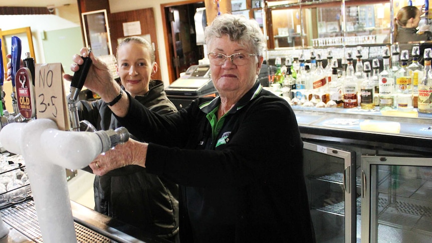 Two women pour beers at a pub while smiling at the camera