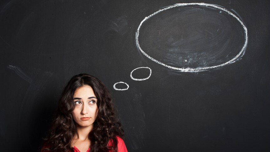 Young woman wears a glum expression and looks up at her thought bubble, chalked in white a black chalk board.