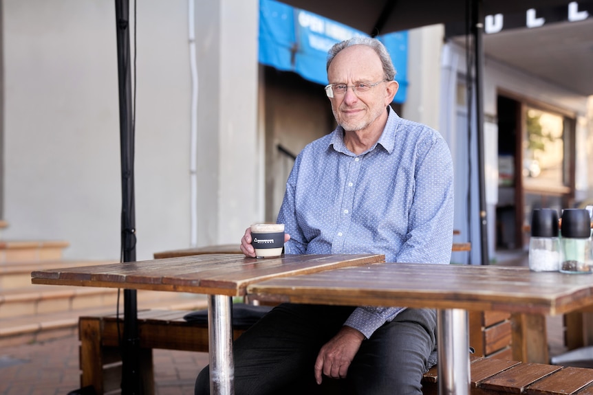 A man sits at a table outside a cafe with a coffee