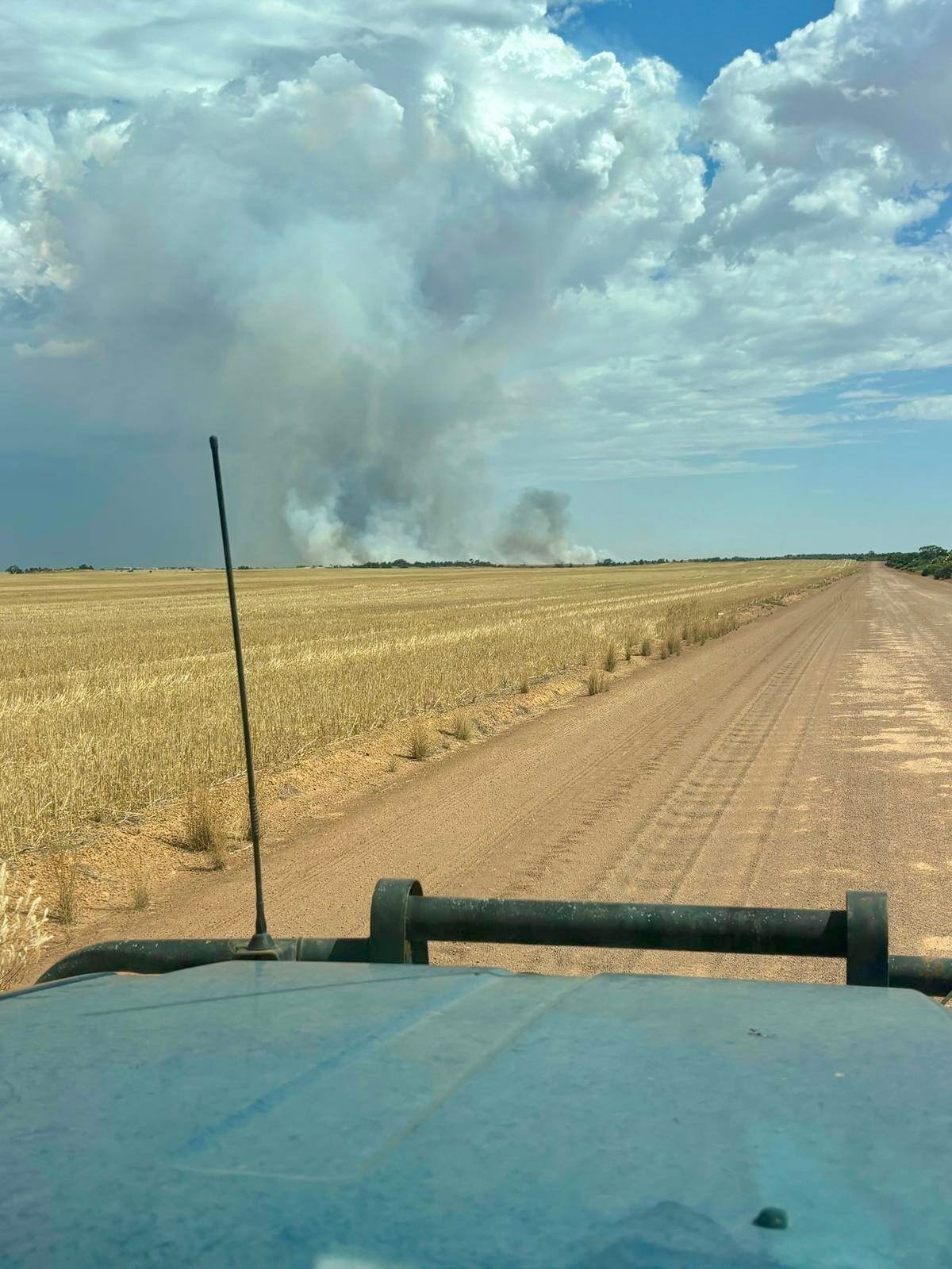 Filmado de dentro de um veículo dirigindo ao lado de uma plantação olhando para a fumaça ao longe. 