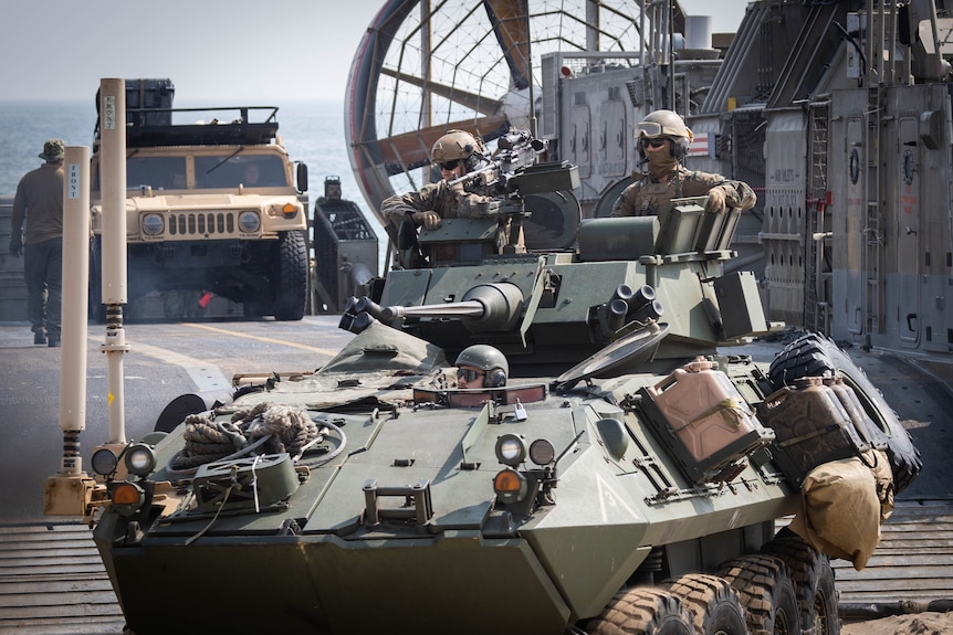 Three soldiers pop their heads up out of a tank, as it disembarks a hovercraft