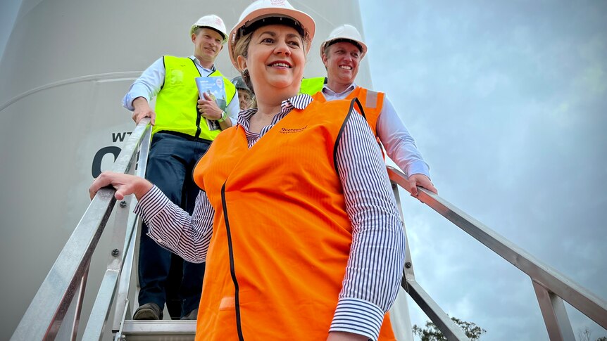 A smiling woman in high-vis and a hard hat – Queensland Premier Annastacia Palaszczuk – descends a flight of stairs/