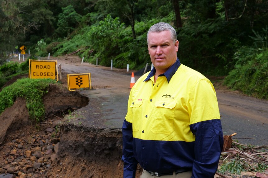 Man in flouros stands by a flood-damaged bush road.