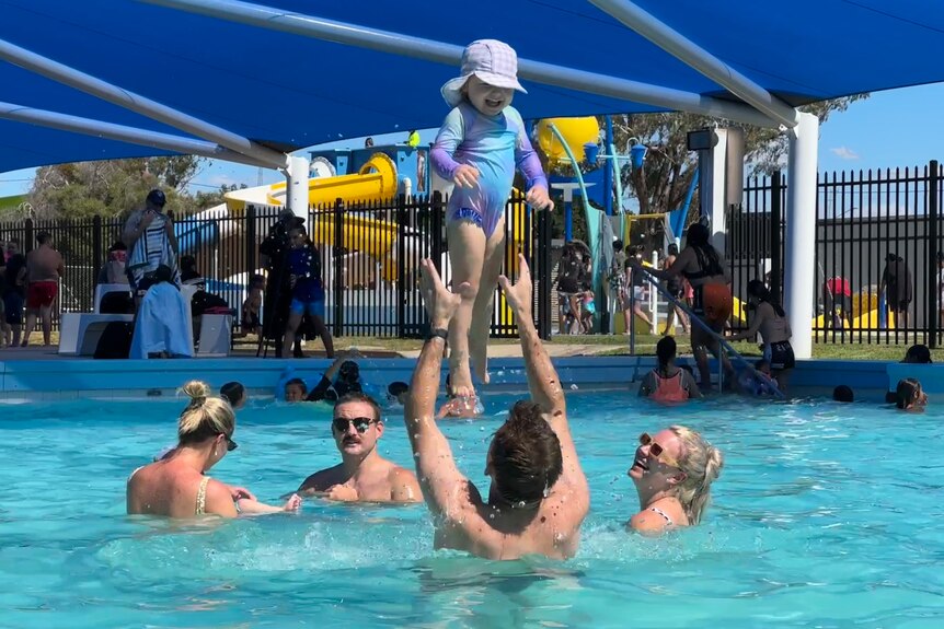 Man in pool throwing his baby in the air.
