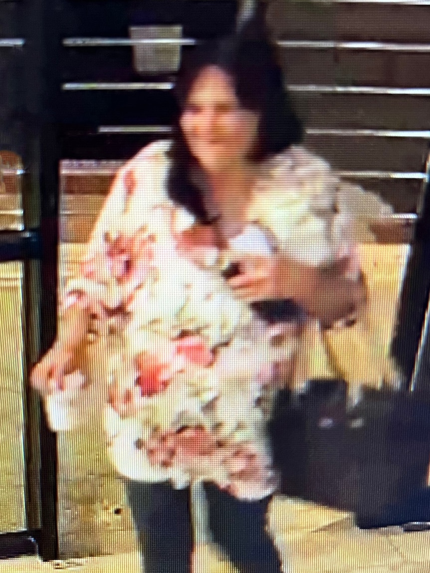 A CCTV still frame showing a woman walking out a door carrying a bag and drink cup.