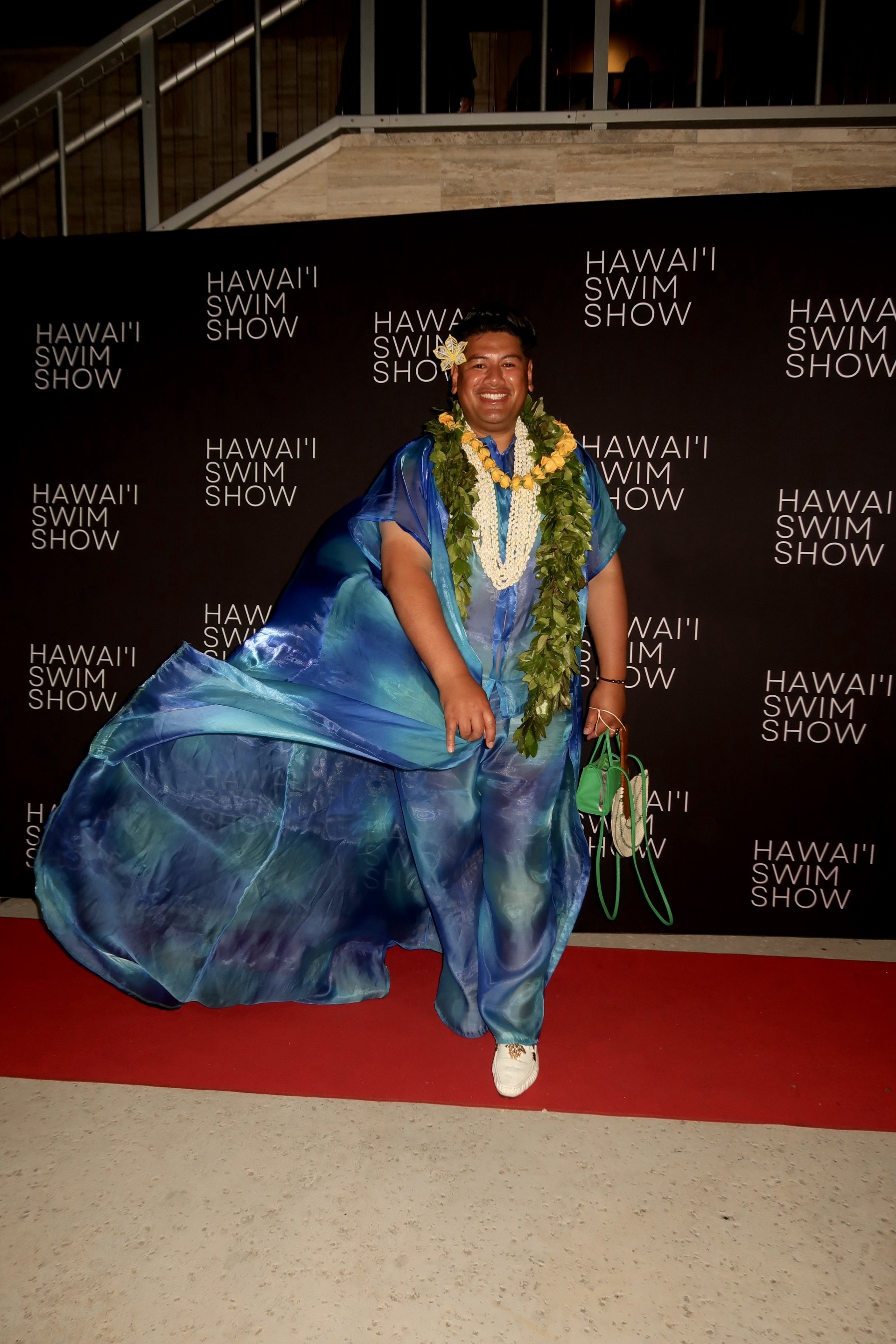A man wearing flowy blue clothes and flowers on a red carpet.