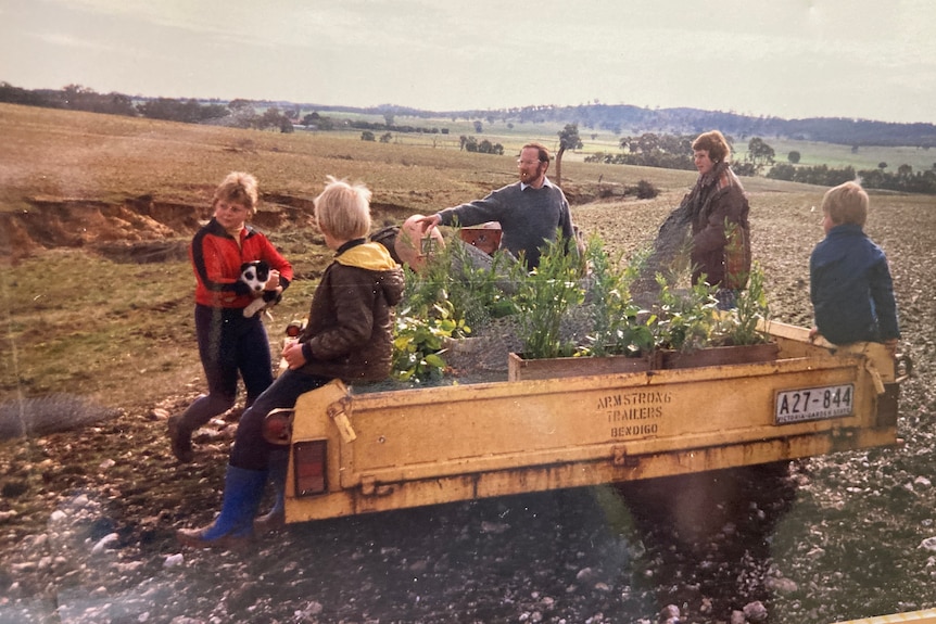 an old photograph showing a man, woman and three children around a trailer full of trees in a rural paddock