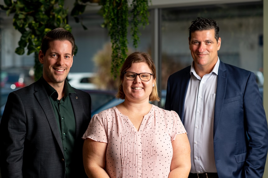 A woman wearing a pink shirt stands in between two men smiling