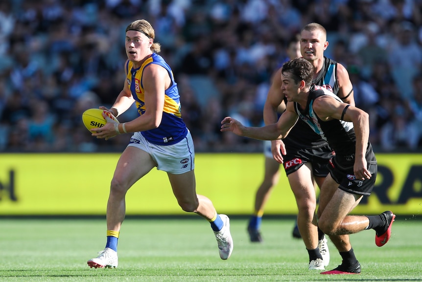 West Coast Eagles AFL player Harley Reid runs with the ball as a Port Adelaide player chases him.