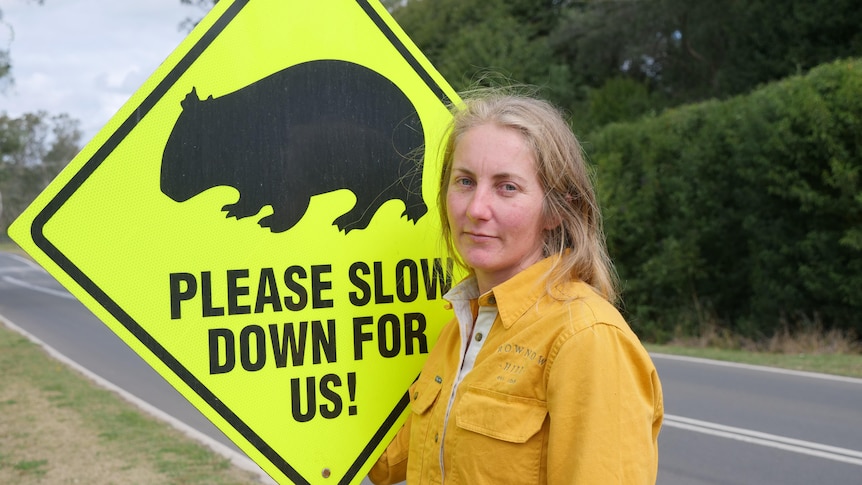 image of woman in yellow work gear in front of sign with a picture of a wombat and slow down warning